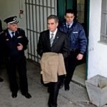 Former Thessaloniki Mayor Vassilis Papageorgopoulos uses a raincoat to hide his handcuffs 