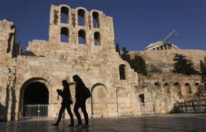 Women walk outside of the ancient Herodes Atticus theatre as the Parthenon temple is seen in the background in Athens