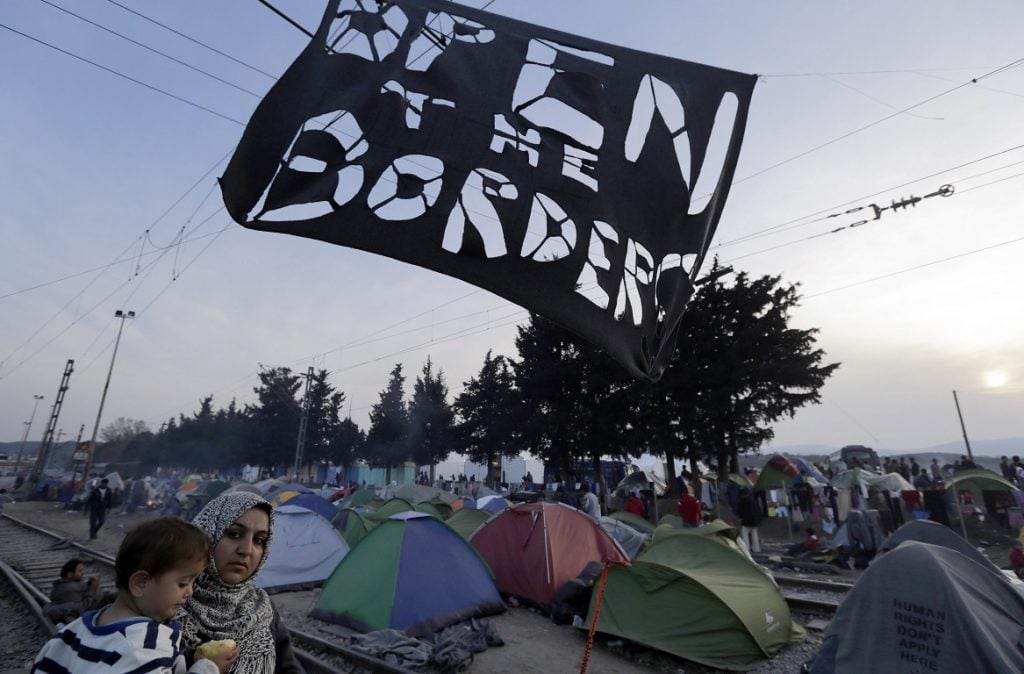 epaselect epa05226246 Migrants and their tents are seen along with a sign reading 'open the border' at the refugee camp on the Greek-Macedonian border, in Idomeni, Greece, 22 March 2016. Migration restrictions along the so-called Balkan route, the main path for migrants and refugees from the Middle East to the EU, has left thousands of migrants trapped in Greece. EPA/ARMANDO BABANI