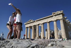 A group of tourists take a selfie in front of the temple of the Parthenon atop the Acropolis in Athens