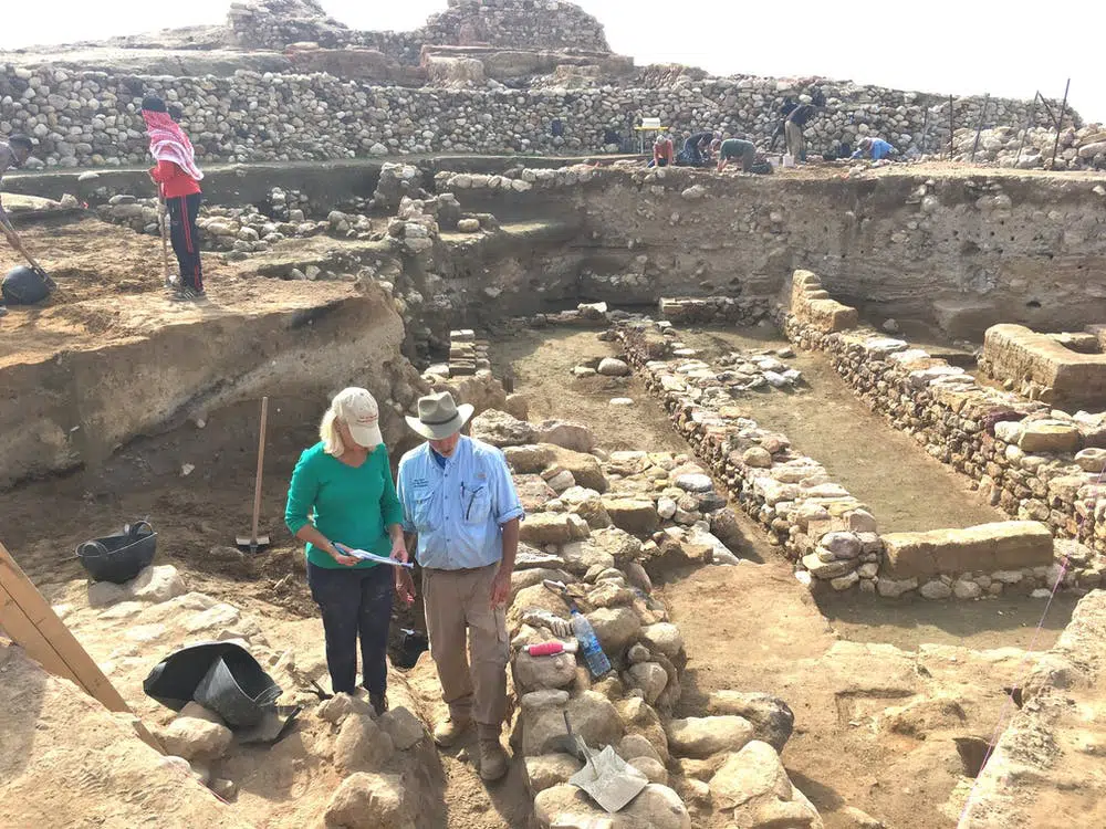 Researchers stand near the ruins of ancient city walls, with the destruction layer about midway down each exposed wall. 