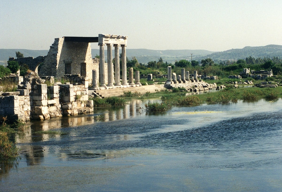 Ruins of ancient Miletus with partially submerged columns and stone structures beneath a clear blue sky. Miletus became a model for the revolutionary grid plan of Hippidamus the Ancient Greek polymath, a system that later influenced urban planning from Alexandria to Manhattan.