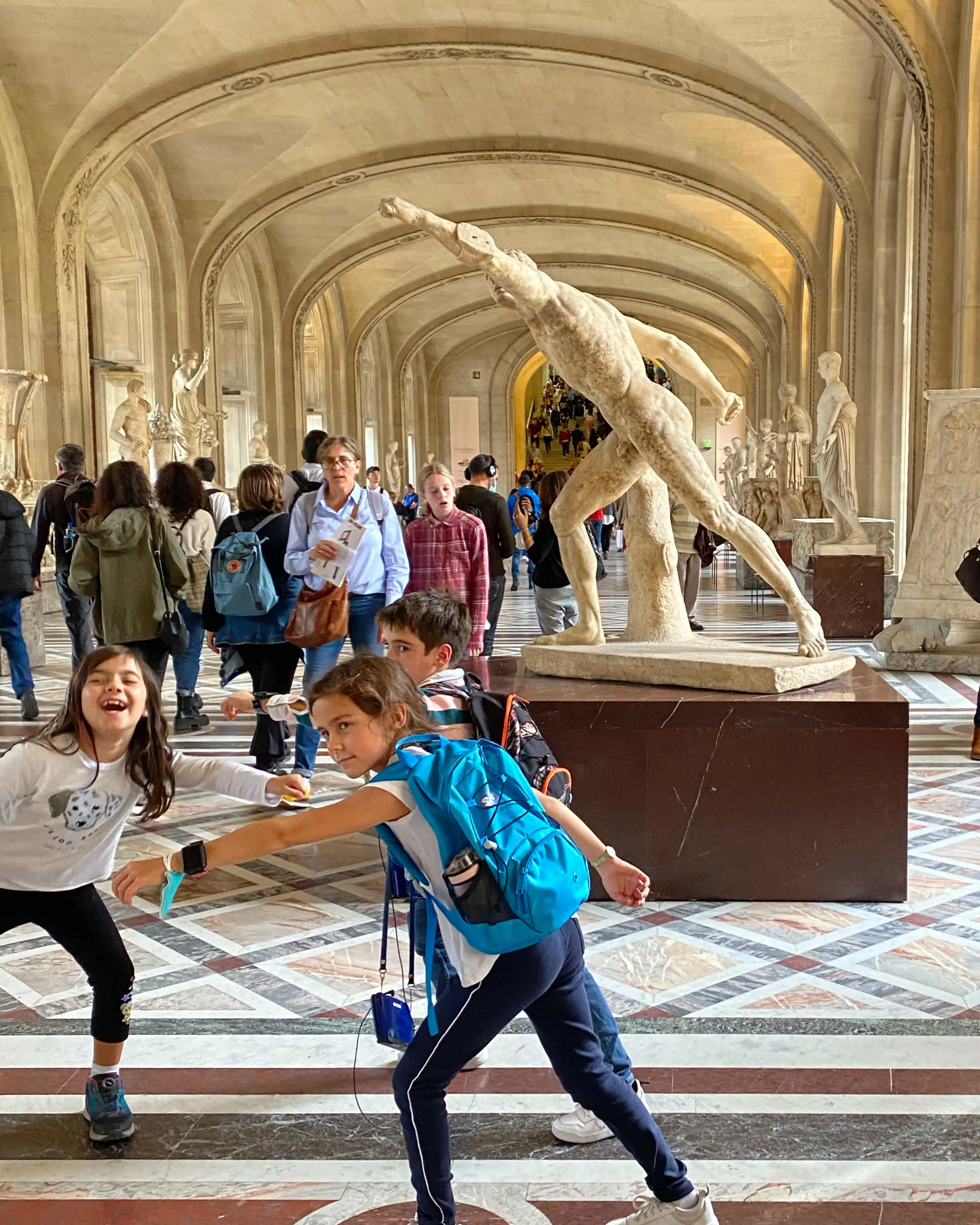Children try to mimic the pose of an ancient Greek statue in Louvre, Paris