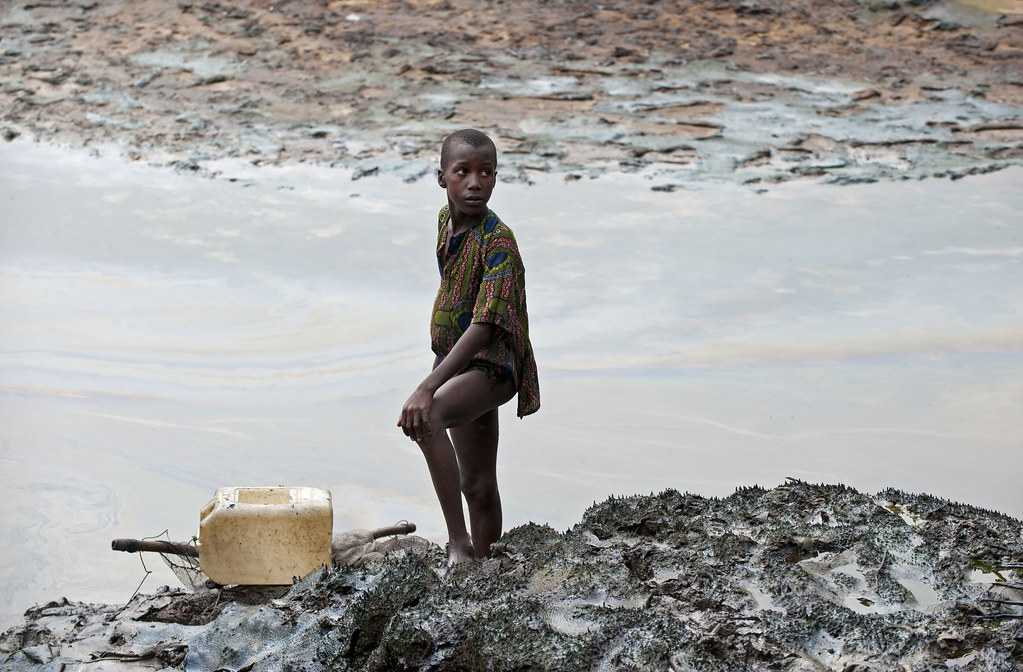 Child standing at oil polluted river banks in Goi