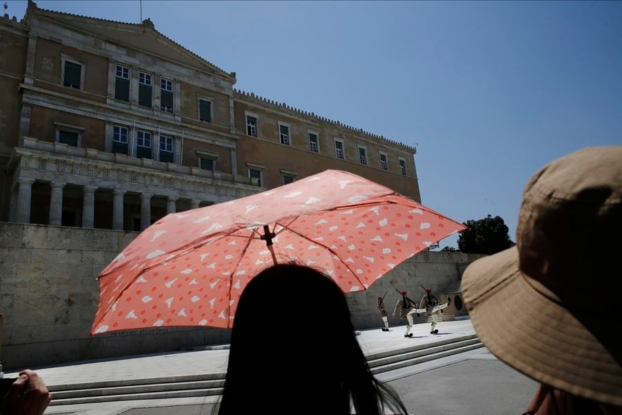 Tourists hold umbrellas to watch the Changing of the Guard Ceremony at Syntagma Square in Athens during a heatwave.