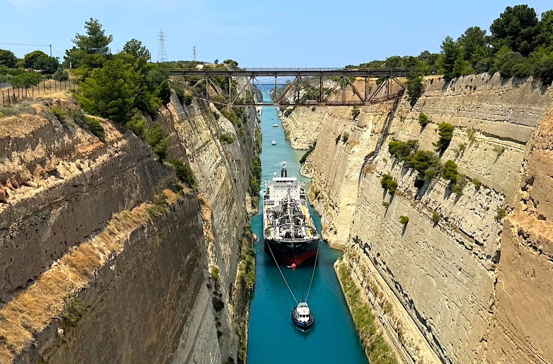 A vessel sails through the narrow Corinth Canal in Greece beneath bridges and steep limestone cliffs.