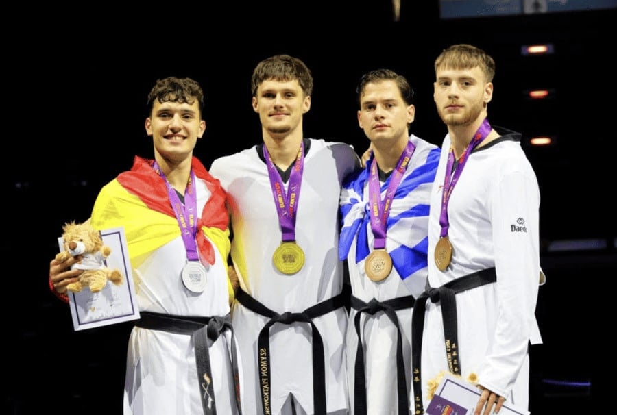 Greek taekwondo athlete Vasilis Tholiotis wearing a bronze medal and draped in the Greek flag on the podium at the European Taekwondo Championship in Munich.