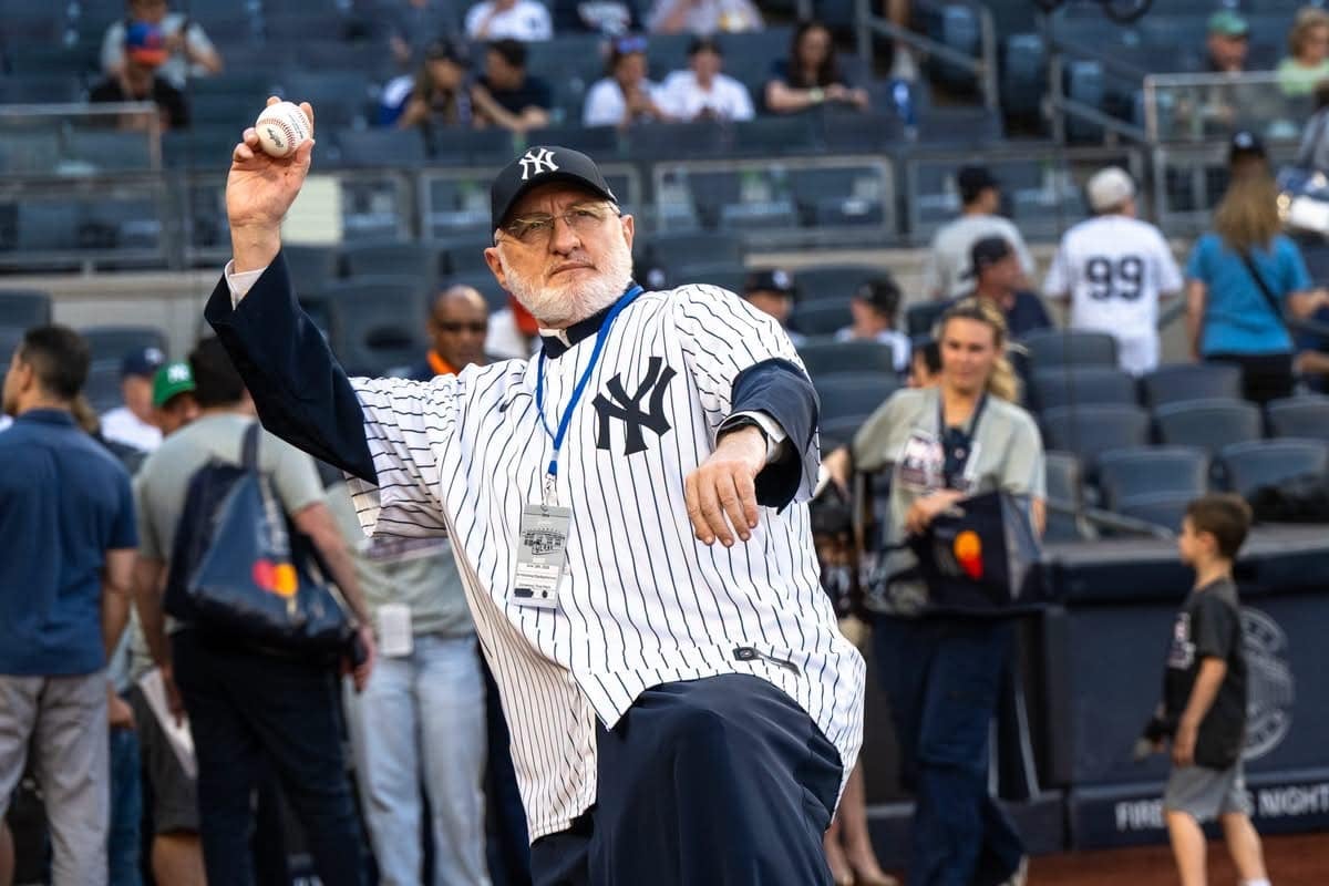 Archbishop Elpidophoros wearing a Yankees jersey and holding a baseball before the ceremonial first pitch at Yankee Stadium.