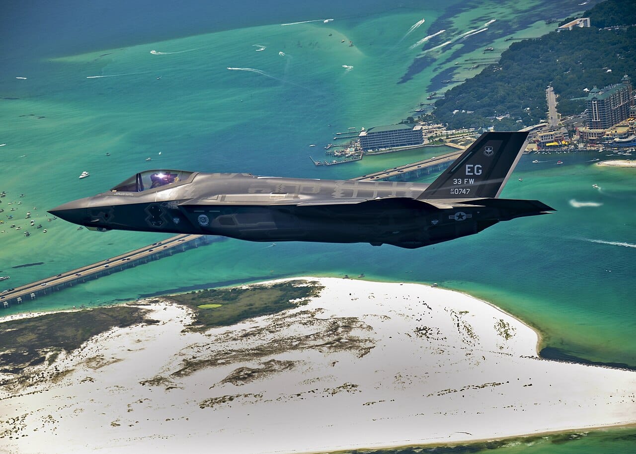 A US Air Force F-35 Lightning II fighter jet flying over a coastal area.