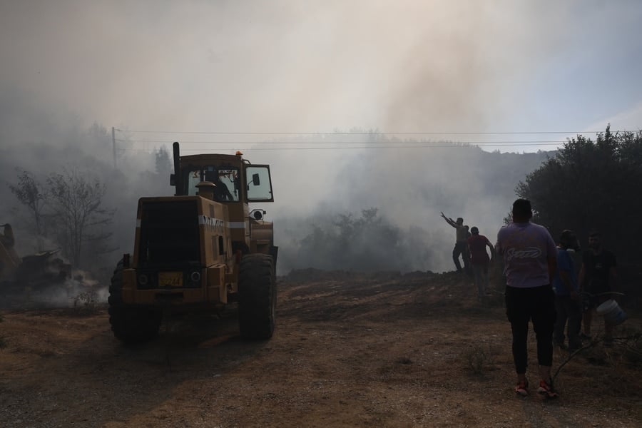 A bulldozer drives through a smoke-filled forest area as people stand nearby during a wildfire near Thessaloniki, Greece.
