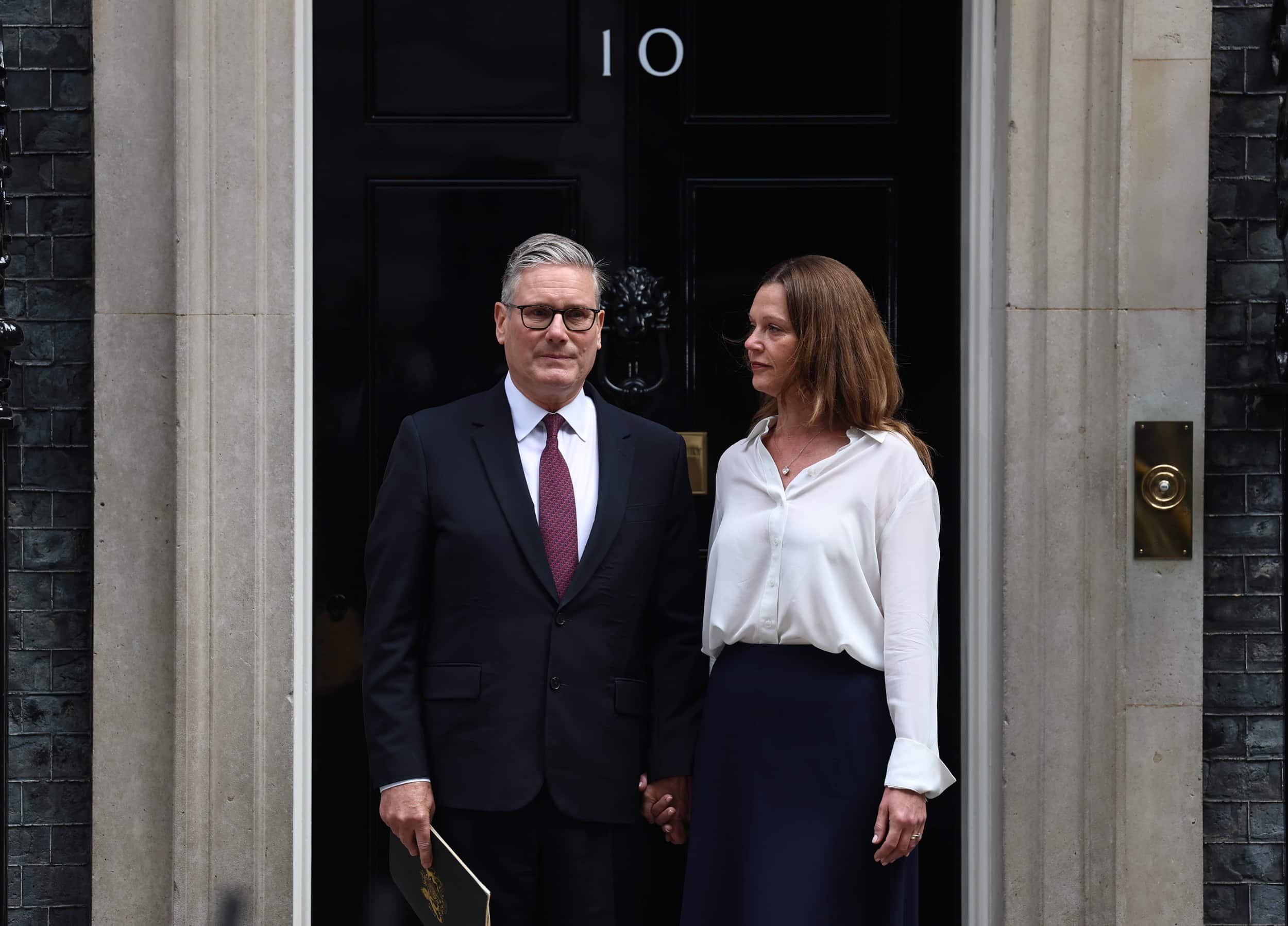 Keir Starmer stands with his wife outside the black door of 10 Downing Street in London.