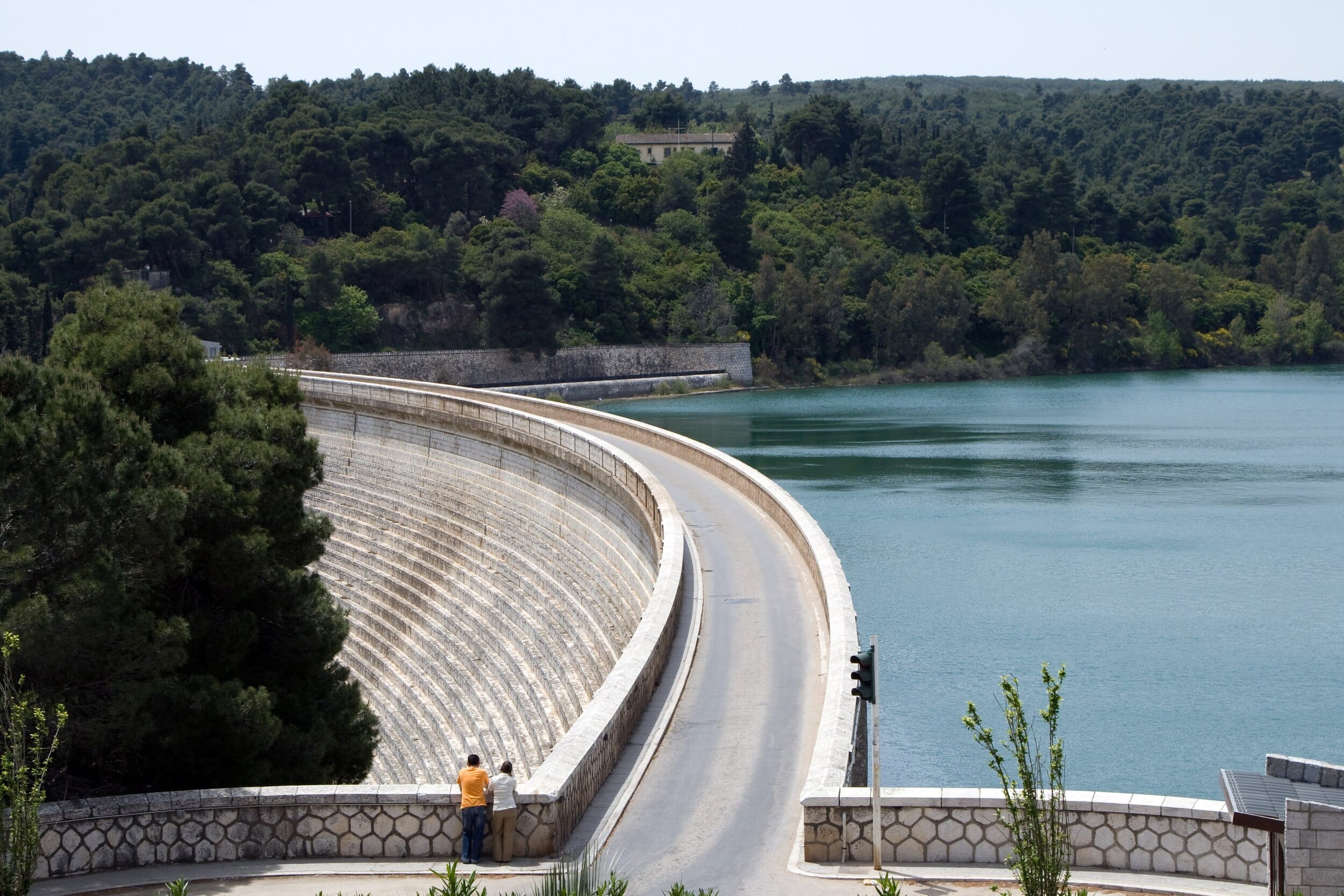 Lake Marathon Dam in Greece, with a curved stone dam wall, reservoir water, and forested hills in the background.