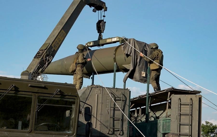Soldiers use a crane to load a large military missile onto a transport vehicle.