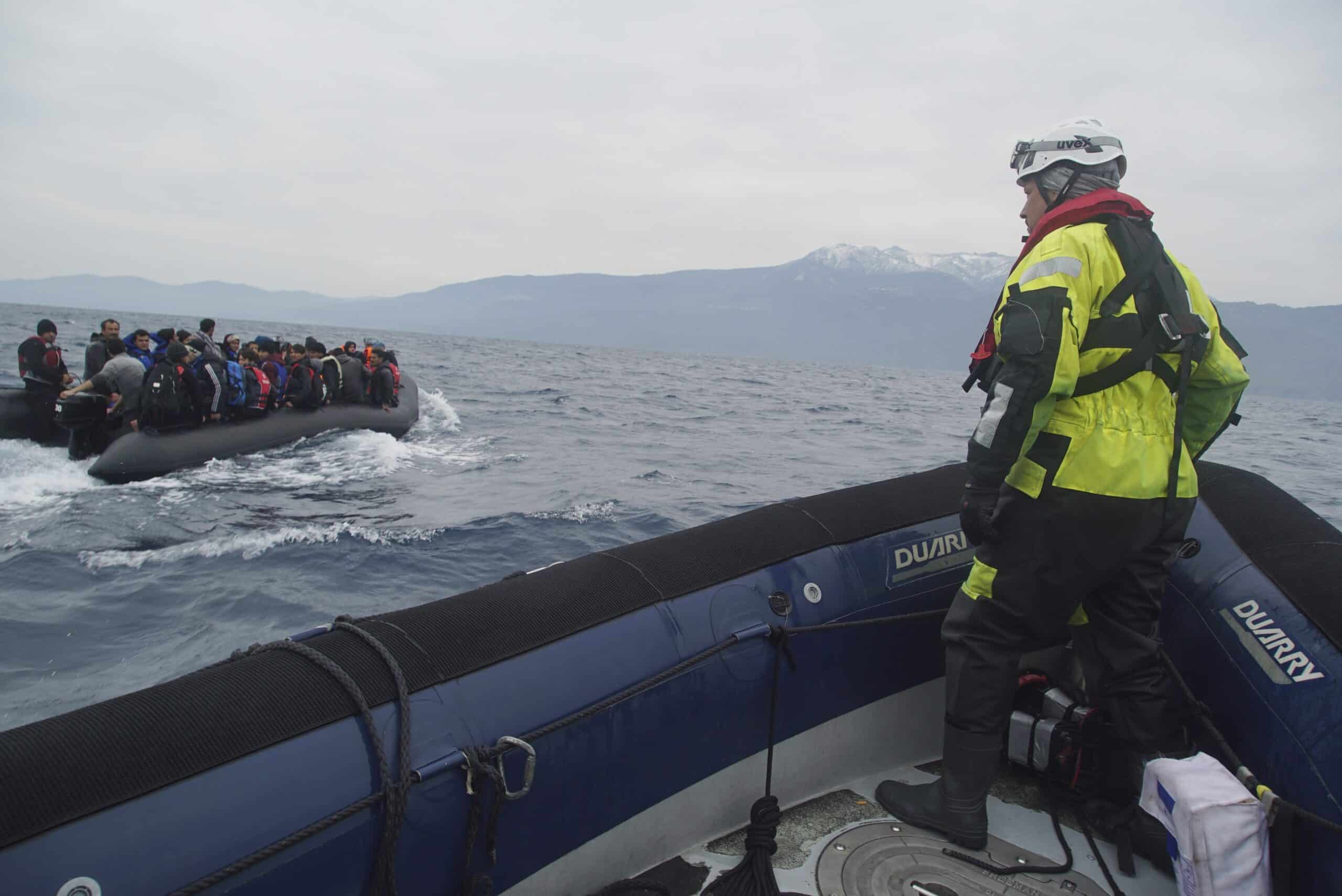 Refugees travel by boat across the Mediterranean Sea toward Greece while a rescue worker watches from a nearby vessel.