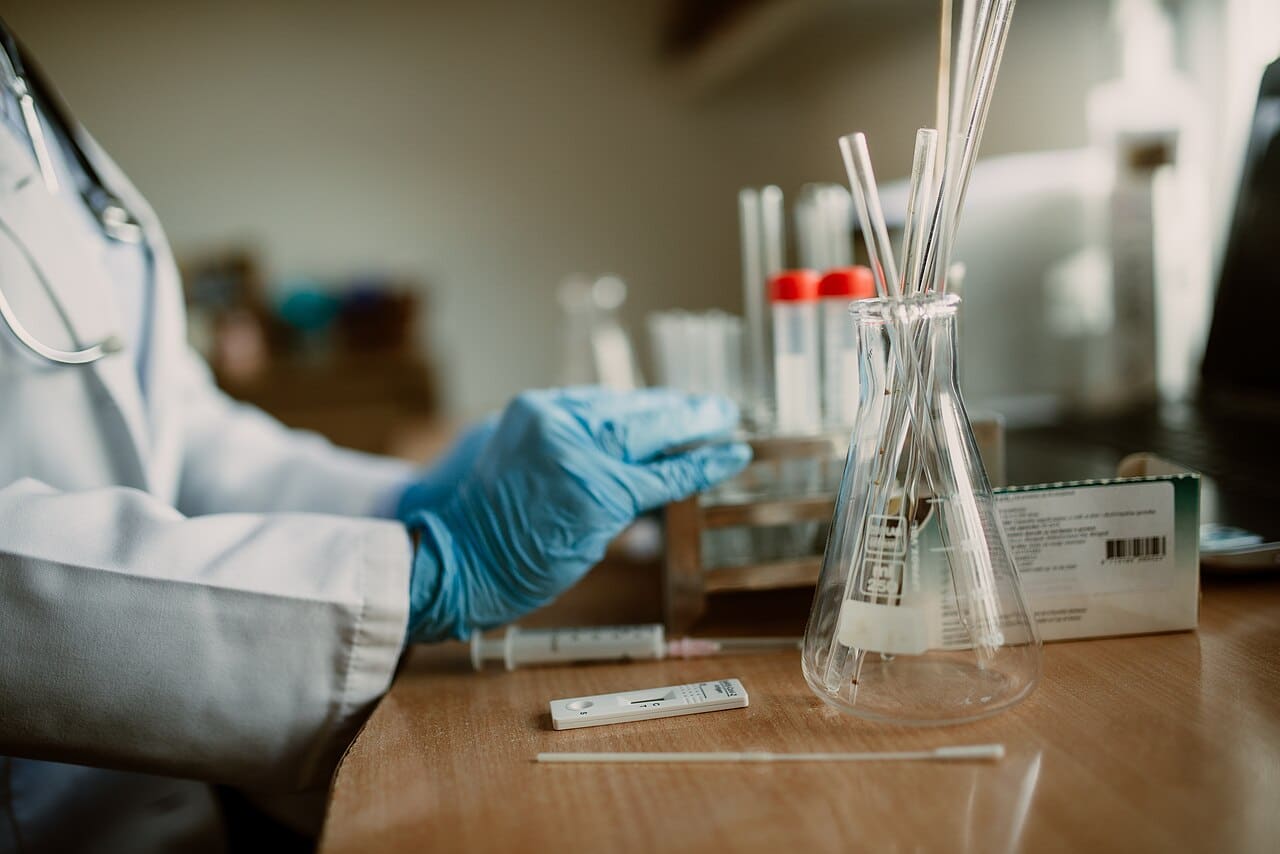 A laboratory researcher wearing blue gloves prepares samples beside test tubes, pipettes, and other scientific equipment.