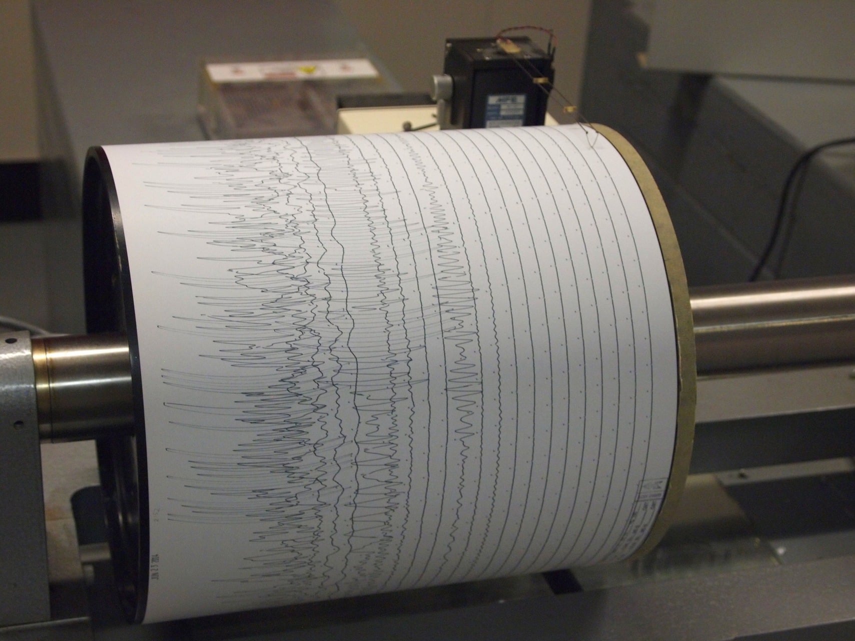Seismograph drum recording earthquake waves on paper in a seismic monitoring station.