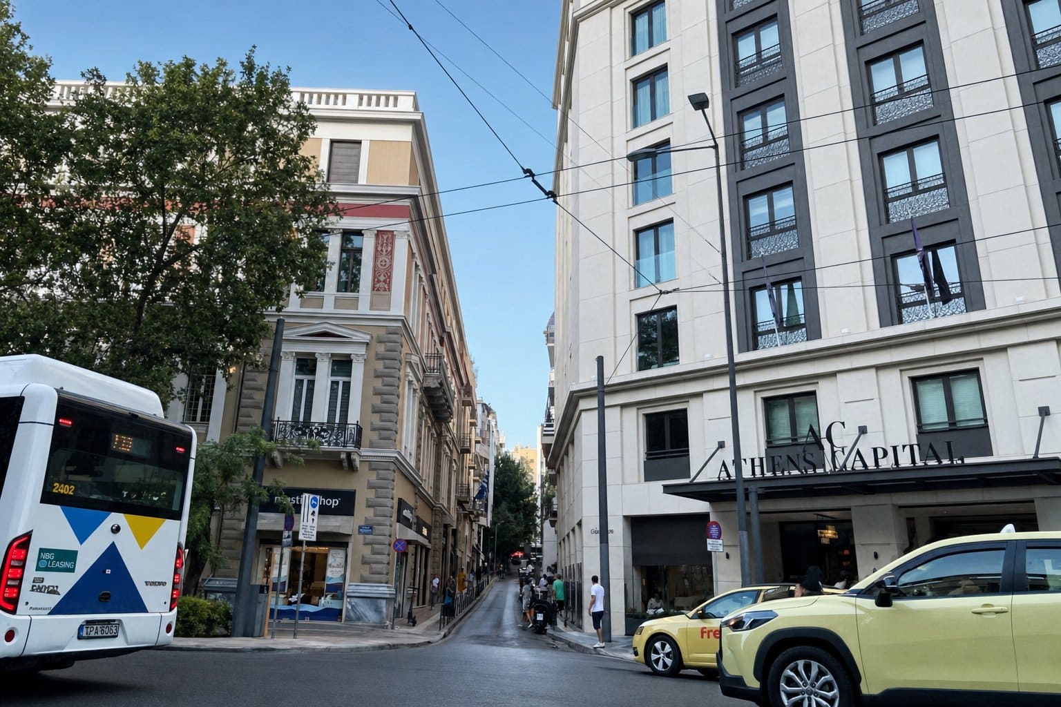Bus and taxis pass the Athens Capital hotel at a city intersection of premium real estate.