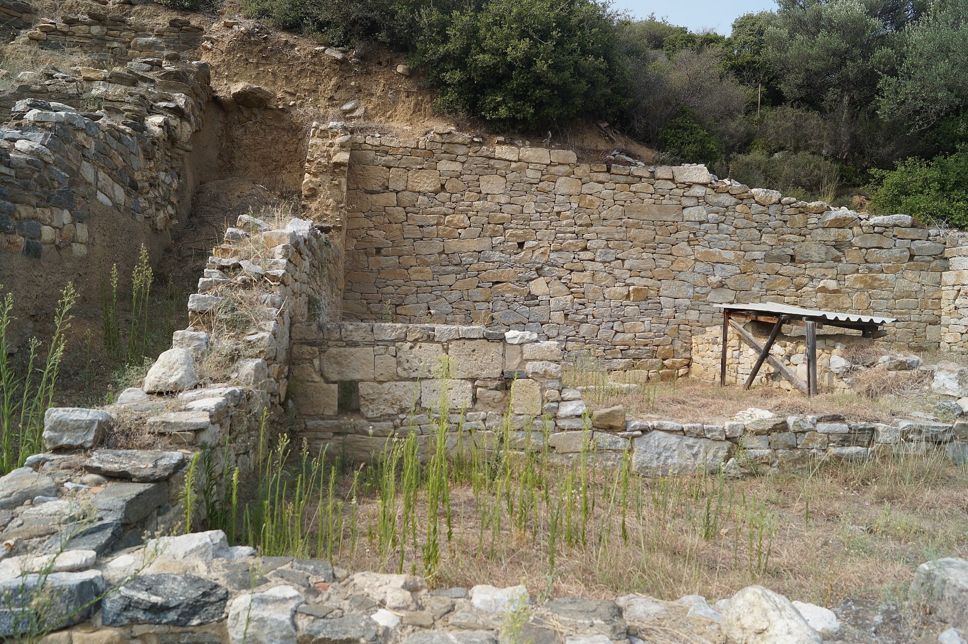 A ground-level photograph captures a partially unearthed archaeological trench showcasing centuries-old stone walls built from stacked limestone blocks.