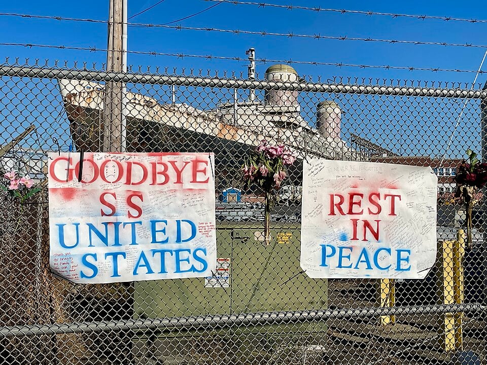 Handwritten farewell signs hang on a fence outside the SS United States as the historic ocean liner awaits its next chapter. The ship, once a record-breaking transatlantic liner, is destined to become an artificial reef off Florida.