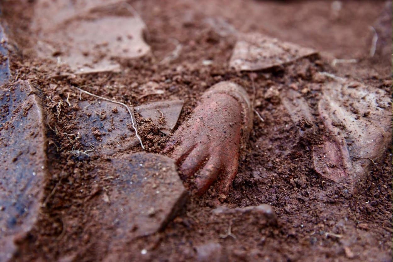 A terracotta hand partially buried in soil during excavations