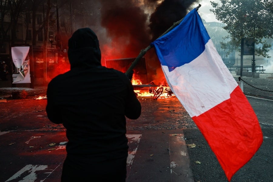 Protester carrying a French flag faces police at Place de la Madeleine in Paris, France during a cost-of-living protest.