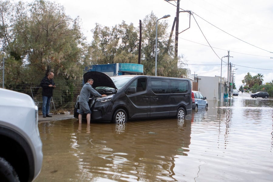 A man attempts to repair a stranded vehicle on a flooded street in Rhodes, Greece, on Wednesday, October 14, 2026, as severe storms and heavy rainfall caused widespread flooding and traffic disruptions. One man was reported dead after his vehicle was swept into the sea during the storm. Photo: Lefteris Damianidis/ANA-MPA